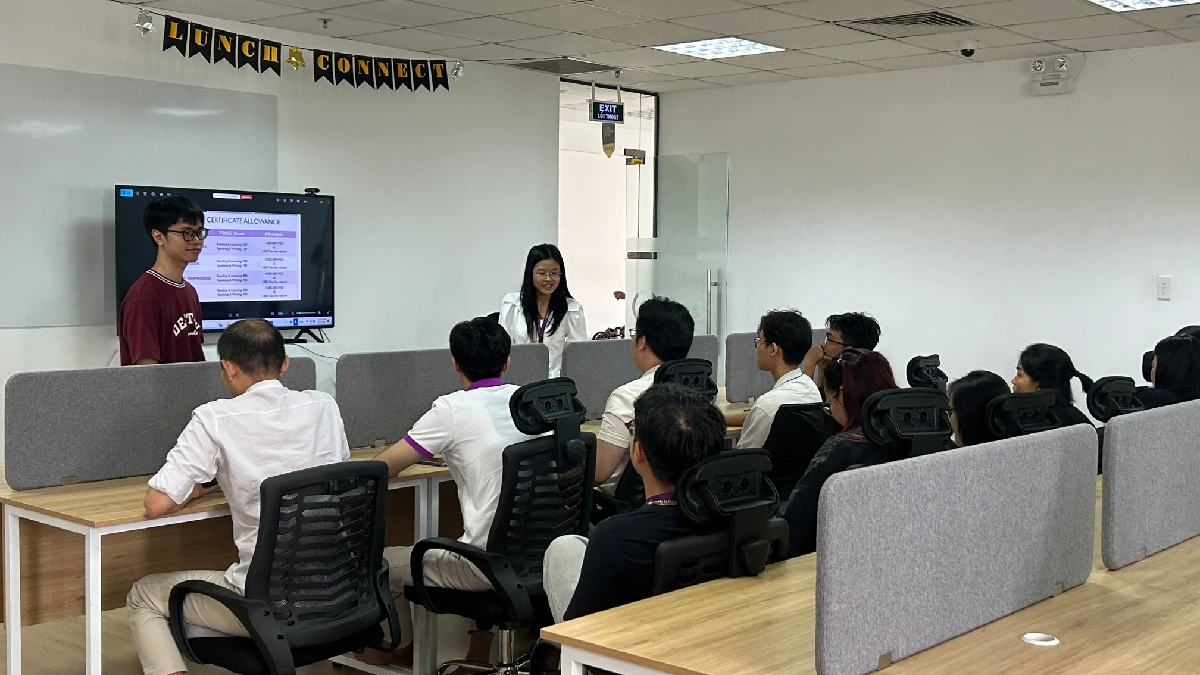 A focused training session in an office setting, with two presenters standing near a monitor displaying slides to a seated audience
