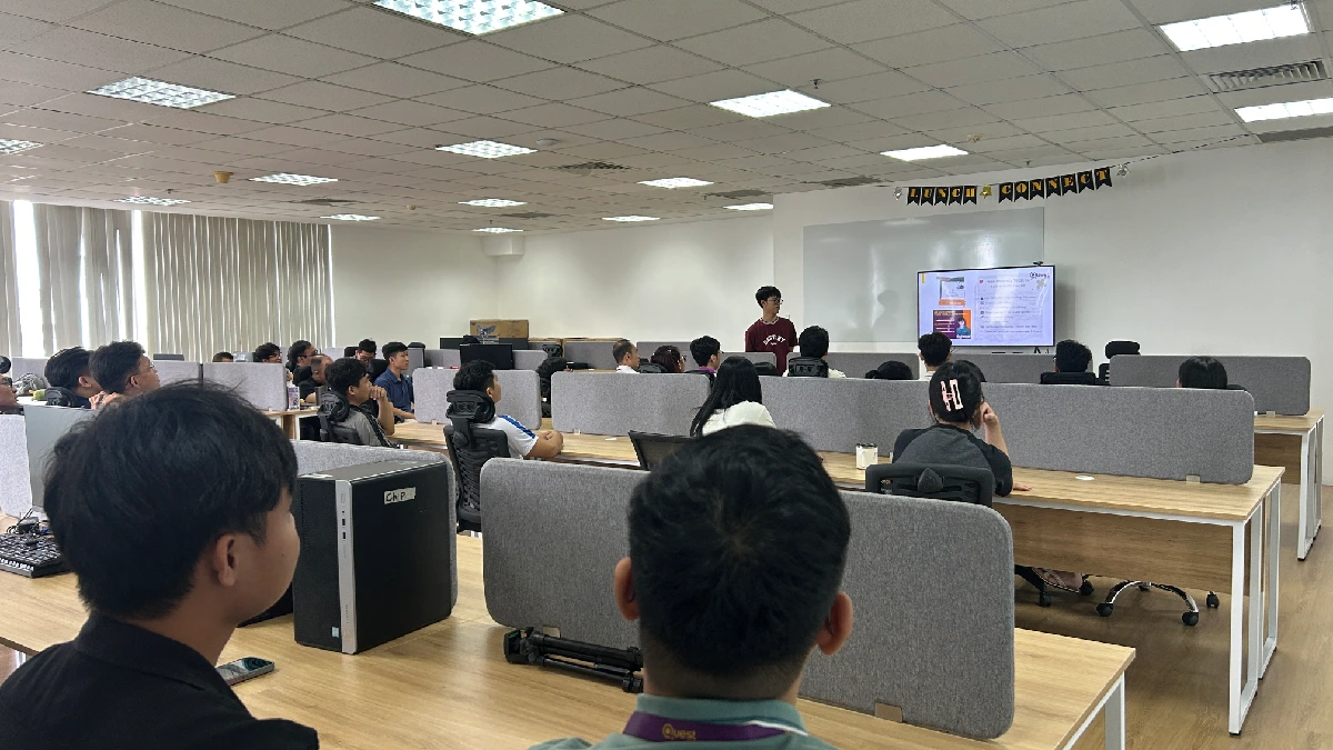 A speaker standing near a large screen displaying slides
