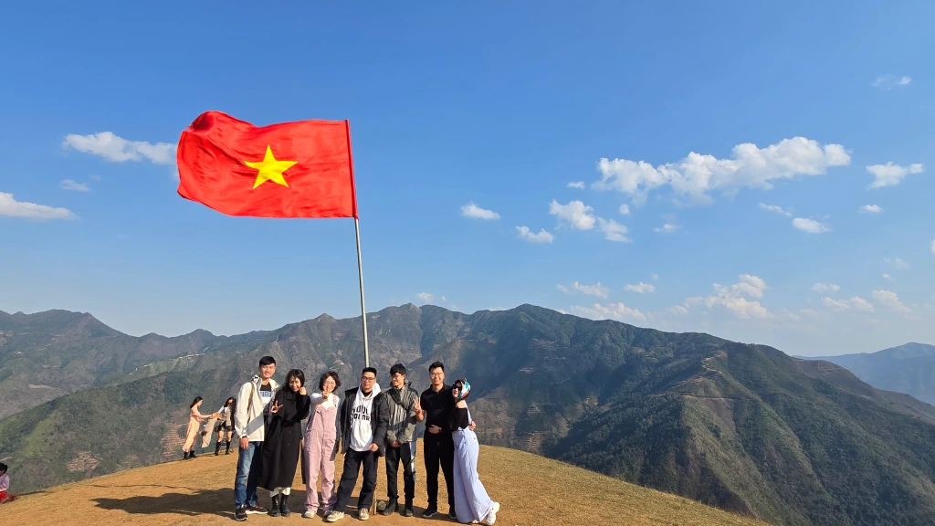 A group of people posing outdoors on a mountain backdrop, holding the Vietnamese national flag during an outing
